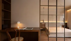 A minimalist bedroom featuring a wooden desk with a table lamp and an open book.