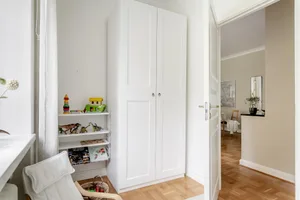 A minimalist white bedroom with wooden floors, white furniture, and a white closet.