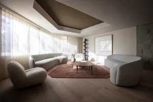 A modern living room with white, curved sofas, a round wooden coffee table, and large windows with sheer curtains.