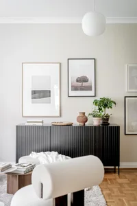 A minimalist living room featuring a black sideboard, white armchair, and various artwork on the wall.