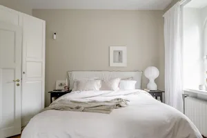 A minimalist bedroom featuring a white bed, white walls, and a white headboard.
