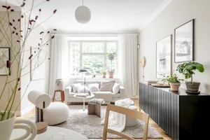 A modern minimalist living room featuring a white sofa, wooden coffee table, and floor-to-ceiling windows with white curtains