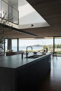 Contemporary kitchen with concrete and glass materials, featuring an island with a sink and a view of the ocean.