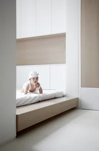A minimalist white interior space with a baby on a bed.