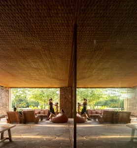 People relaxing in a bamboo lounge area with plush seating and open windows.
