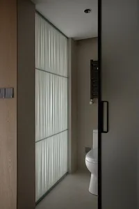 A minimalist bathroom with a glass shutter door and a white toilet, featuring a sleek, modern design.