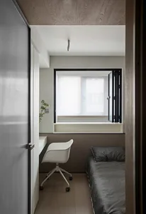 A minimalist bedroom featuring a grey twin bed, window, and white office chair.