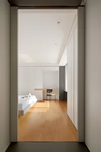 A minimalist bedroom with white walls, a wooden floor, and furniture.