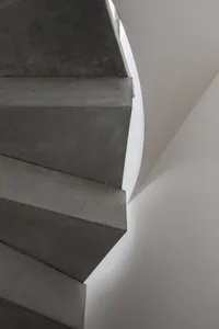 A sleek, modern concrete staircase with a curved wall and white ceiling in an interior setting.