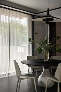 A modern dining room featuring a round black marble table and sleek white chairs under a contemporary pendant light.