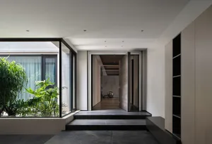 A modern entrance hall with a concrete floor and a large window overlooking a lush garden.