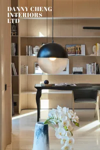 Modern home office featuring a wall of built-in bookshelves and wood furniture, with a pendant light fixture hanging above a 