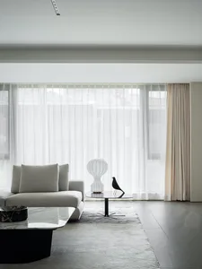 Modern living room featuring a glass coffee table, a stone floor, and white sheer curtains.