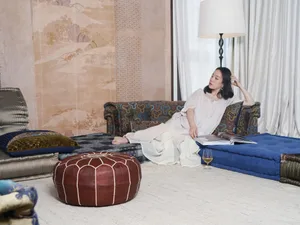 A woman relaxes on a stylish modern living room sofa adorned with various colorful textiles and decorative elements like a la