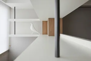 A modern wooden shelf with a white bird figurine on it, located next to a window with blinds.