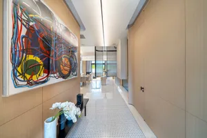 A minimalist modern interior hallway with a large abstract painting on the left and a minimalist bench with orchids and vases