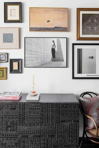 A wall adorned with various framed artworks, including a black-and-white photo of a woman and a painting of an elephant.