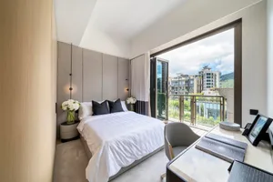 Modern bedroom featuring white furniture, grey walls, and a balcony view of urban buildings.