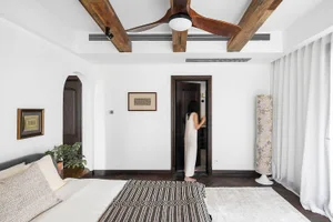 A modern bedroom with a wooden ceiling fan, white walls, and a white rug with black patterns.