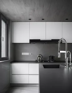 A modern kitchen featuring concrete walls and marble countertops with white cabinets and appliances.