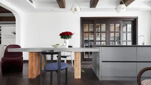 A modern kitchen featuring concrete countertops and wooden baseboards with a vase of red roses on the table.