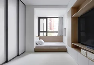 A minimalist bedroom with a bed platform, window, and built-in shelves.