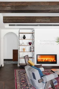 A minimalist living room featuring a wooden fireplace, bookshelf, and comfortable seating area on a patterned rug.