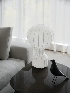 Modern living room with a sleek grey sofa, white fabric lampshade on a glass table, and a black bird figurine.