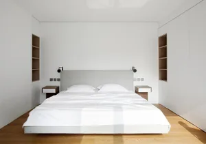Minimalist floating bed platform with white bedding and black lamps in a white-walled bedroom with wooden flooring.