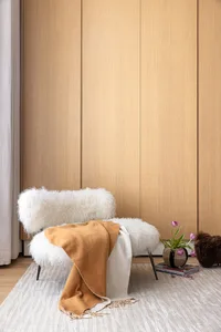 A cozy modern living room with a plush white bench adorned with a warm orange throw blanket, set against a wooden wall and a