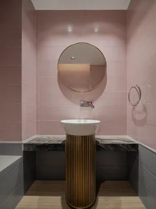 A minimalist bathroom with pink ceramic tiles, a round mirror, and a modern sink with a gold stand.