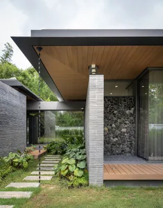 Modern house exterior featuring a stone and concrete entrance with a wooden overhang and greenery.