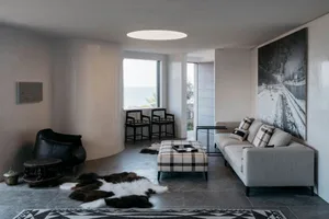 A modern living room featuring a minimalist interior design with concrete walls and floor, a large sofa, and large windows wi