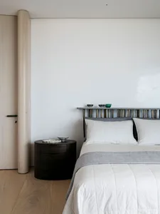 A minimalist bedroom featuring a bed with a wooden headboard, a metal shelf, and fabric bedding.