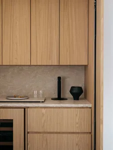 A minimalist kitchen features wooden cabinets and a marble countertop with a sleek black faucet and decorative black vase.