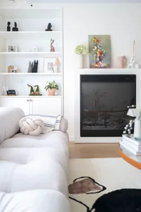 A minimalist residential interior featuring a white wall with built-in shelves, a modern fireplace, and a cozy seating area.