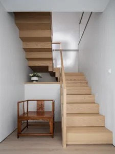 A minimalist staircase made of light-colored wood with a single wooden chair next to it.
