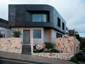 A modern residential house featuring black metal exterior walls, brick details, and a stone wall.
