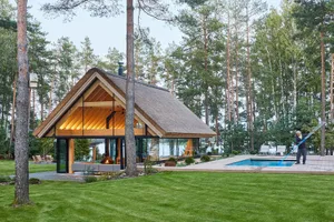 Modern holiday home featuring a thatched roof, glass windows, and a swimming pool surrounded by greenery.