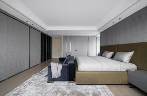 A minimalist bedroom featuring a beige leather bed against a gray wall, with a blue velvet sofa and a textured rug.