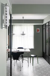 Modern minimalist dining room with concrete table and chairs, large window with sheer curtains, and green stool.