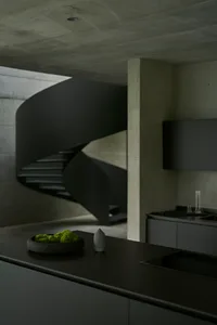 A modern minimalist kitchen with a spiral staircase in concrete.