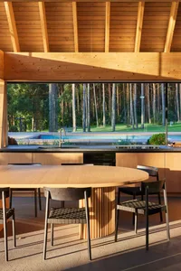 A modern minimalist kitchen with wooden elements and a view of a forest through the large window.
