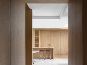 A modern minimalist kitchen with wooden cabinets and stools, featuring a clean and functional design.