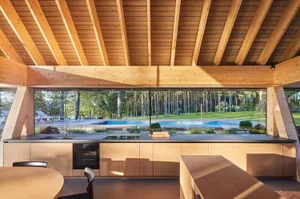 Modern outdoor kitchen with wooden elements and a swimming pool in the background.