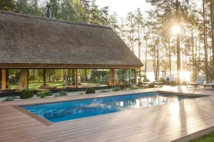 Modern residential building featuring wood and thatch exterior, glass walls, and pool.