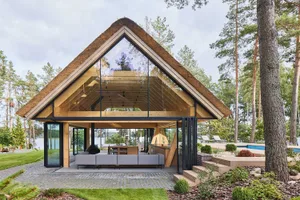 A modern vacation home featuring a thatched roof, glass walls, and wooden interior.
