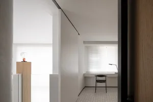 A minimalist white office space with a desk, chair, and light fixture.