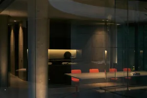Interior of a minimalist conference room with a long table, red chairs, and concrete walls.