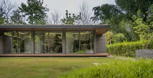 A modern house with large glass windows and a flat roof, surrounded by greenery.